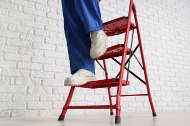 Beyaz tuğla duvarın yanındaki merdivenden inen kadın işçi.