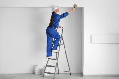 Merdiven fırçasıyla oda duvarını boyayan kadın işçi.