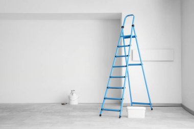 Odada ışık duvarının yanında boya kutuları olan mavi merdiven.