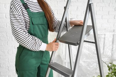 Beyaz tuğla duvarın yanında merdiveni olan kadın işçi.