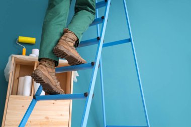 Mavi duvarın yanındaki merdivende kadın işçi, yakın plan.