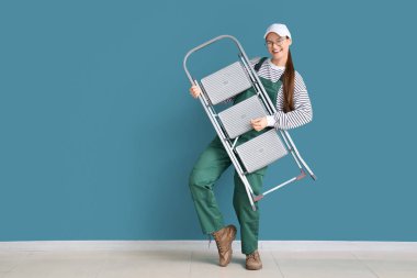 Mavi duvarın yanında merdiveni olan kadın işçi.