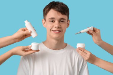 Sivilceli ve kadın elli genç çocuk mavi arka planda cilt ürünleri tutuyor.