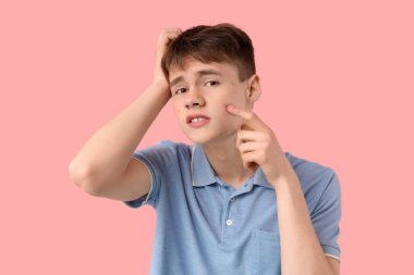 Pembe arka planda sivilceli genç bir çocuk.