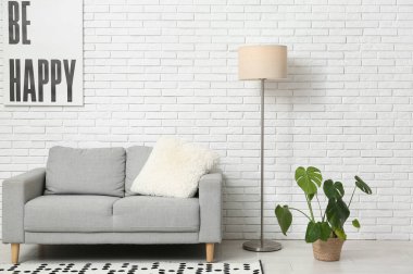 Aydınlık oturma odasında yerde lamba olan gri kanepe.