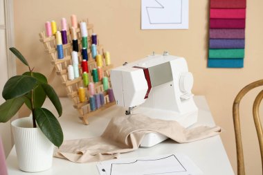 Atölyede terzi masasında kumaşlı dikiş makinesi, yakın plan.