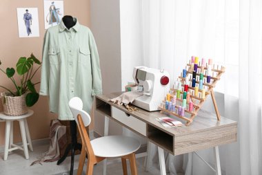 Atölyenin penceresinin yanındaki dikiş makinesi ve iplik makarasıyla terzinin işyeri