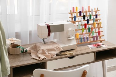 Atölyenin penceresinin yanındaki dikiş makinesi ve iplik makarasıyla terzinin işyeri