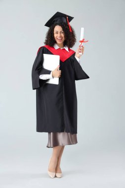 Beyaz arka planda diploması ve dizüstü bilgisayarı olan mutlu Afro-Amerikan bayan mezun.