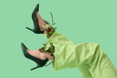 Yeşil arka planda güzel çiçekleri olan şık topuklu genç kadınların bacakları.