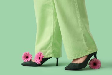 Yeşil arka planda güzel Gerbera çiçekleri olan şık topuklu genç kadınların bacakları.