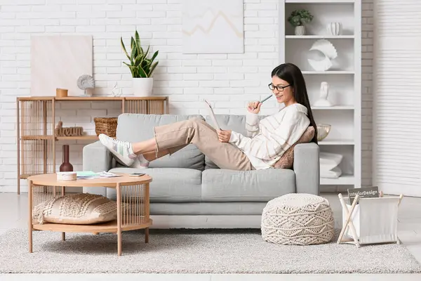 Modern tabletle çalışan ve oturma odasındaki kanepede oturan güzel genç bir kadın.