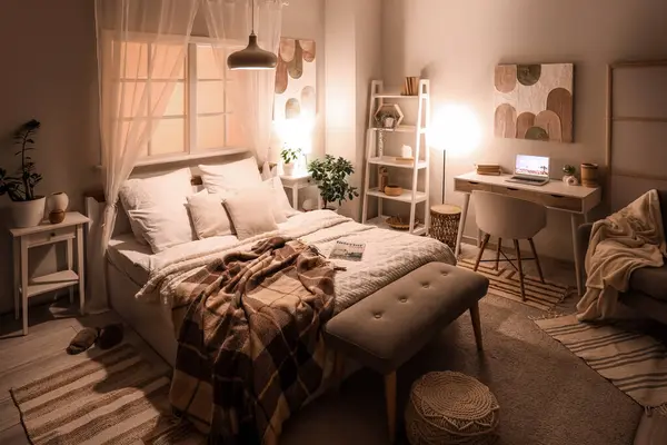 Gece geç saatlerde iş yerinde parlak lambalar ve dizüstü bilgisayarı olan şık bir yatak odası.