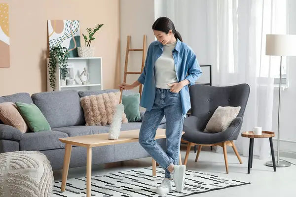 Genç kadın oturma odasında pp-toz ile masayı temizliyor.