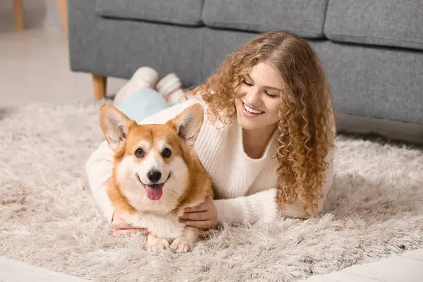 Evde yerde yatan sevimli Corgi köpeği olan genç bir kadın.