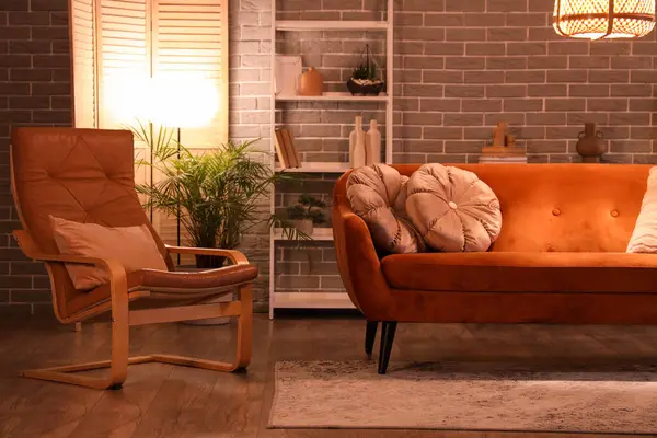 Modern oturma odasının içinde kırmızı kanepe, koltuk, raf ünitesi ve akşamları parlayan lambalar.