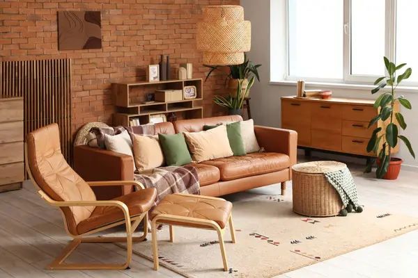 Oturma odasının içinde deri kanepe, koltuk, hasır sepet ve raf ünitesi var.