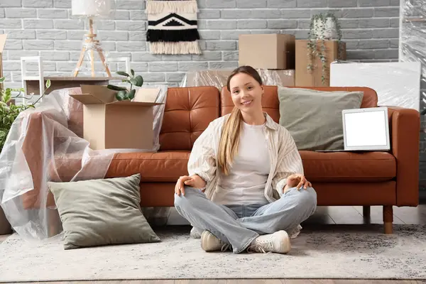 Taşındığı gün boş dizüstü bilgisayarla kanepenin yanında oturan genç bir kadın.