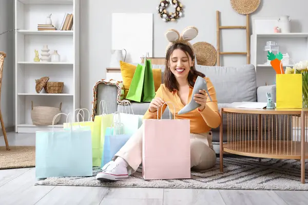 Tavşan kulaklı genç bir kadın Paskalya Günü 'nde evde alışveriş torbasından yüksek topuklu ayakkabı alıyor.
