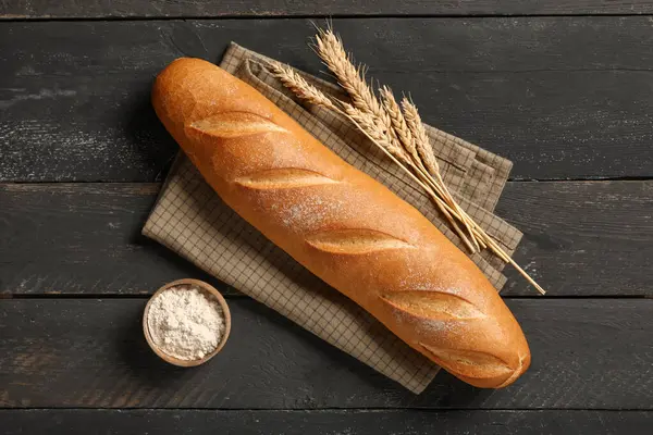 Buğdaylı taze baget ve siyah ahşap arka planda bir kase un.