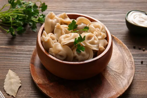 Bir kase lezzetli maydanozlu haşlanmış hamur köftesi ve ahşap arka planda ekşi krema, yakın plan.