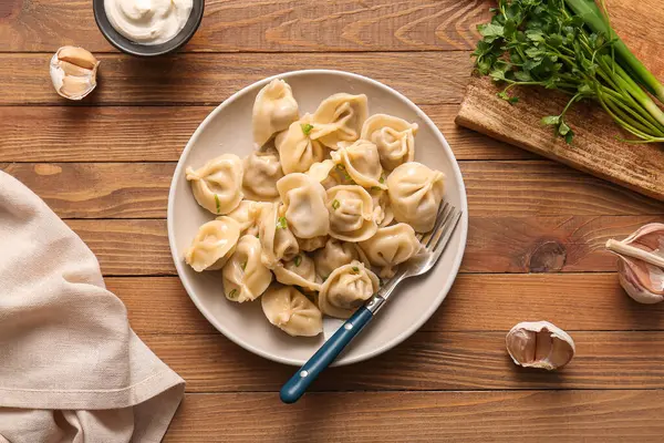 Maydanozlu kaynamış hamur köftesi ve ahşap zemin üzerinde bir kase ekşi krema.