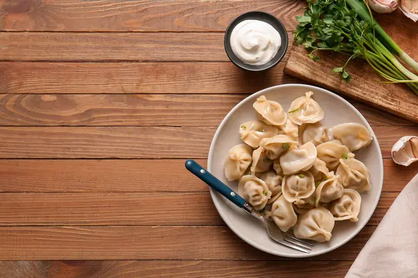 Maydanozlu kaynamış hamur köftesi ve ahşap zemin üzerinde bir kase ekşi krema.