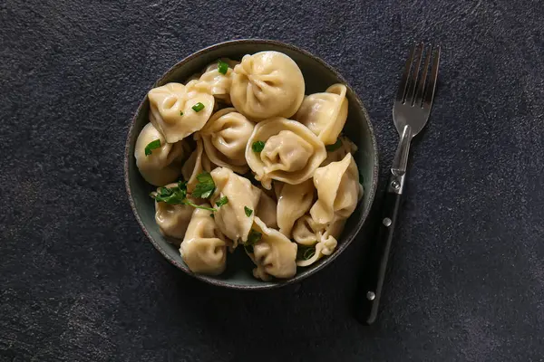 Koyu arkaplanda yeşil soğanlı ve maydanozlu bir kase lezzetli haşlanmış hamur köftesi.