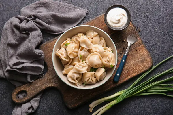 Koyu arkaplanda yeşil soğanlı ve ekşi kremalı bir kase lezzetli haşlanmış hamur köftesi.