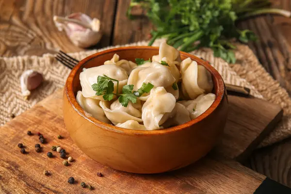 Tahta arka planda maydanozlu ve sarımsaklı bir kase lezzetli haşlanmış hamur köftesi.