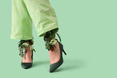 Yeşil arka planda güzel çiçekleri olan şık topuklu genç kadınların bacakları.