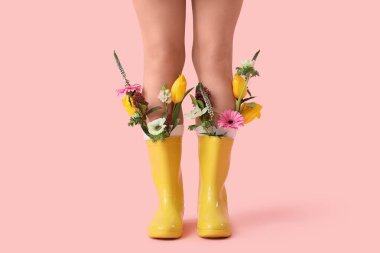 Pembe arka planda güzel çiçekleri olan kauçuk çizmeli genç kadın bacakları.