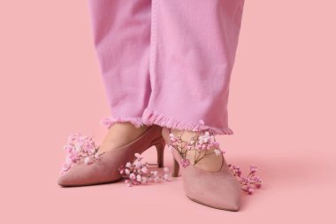 Pembe arka planda güzel çigila çiçekleri olan şık topuklu genç kadınların bacakları.