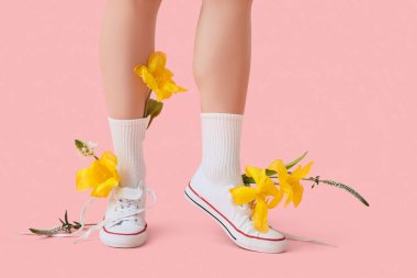 Pembe arka planda güzel çiçekleri olan şık beyaz spor ayakkabılı genç kadın bacakları.