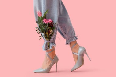 Pembe arka planda güzel çiçekleri olan gri topuklu genç kadın bacakları.