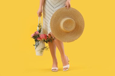 Elinde güzel karanfil çiçekleri ve sarı arka planda ağaç dalları olan ip torbası tutan genç bir kadın.