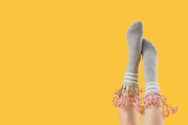 Sarı arka planda güzel çigila çiçekleri olan gri çoraplı genç kadın bacakları.