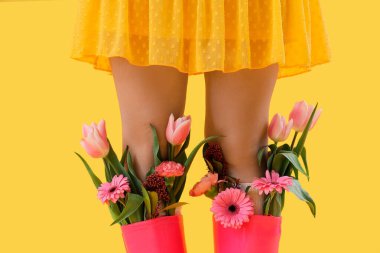 Sarı arka planda güzel çiçekleri olan kauçuk çizmeli genç kadın bacakları.