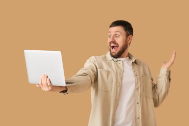 Bej arka planda dizüstü bilgisayarı olan şaşırmış genç bir adam.