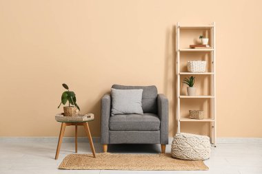 Zarif gri koltuk, yumuşak puf ve bej duvarın yanındaki masa.