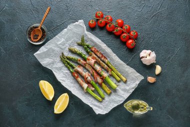 Koyu arkaplanda pastırma ve malzemelerle pişmiş yeşil kuşkonmaz kağıdı.