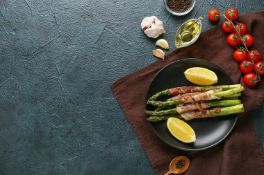 Koyu arkaplanda domuz pastırmalı ve limonlu kızarmış yeşil kuşkonmaz.