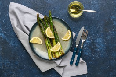 Kızarmış yeşil kuşkonmaz ve mavi arka planda limon dilimleri.