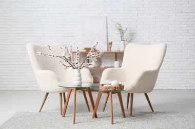 Oturma odasının içinde koltuklar, masalar ve çiçek açan dallar.