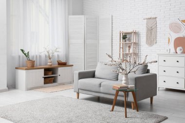 Oturma odasının içinde kanepe ve çiçek açan dallar var.