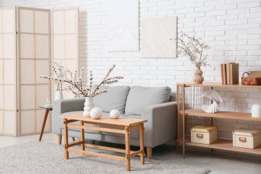 Oturma odasının içinde kanepe, masa, katlanır perde ve çiçek açan dallar.