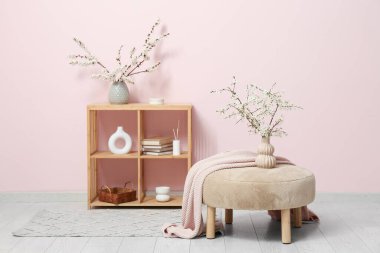 Odanın içinde raflar, puf ve çiçek açan dallar var.