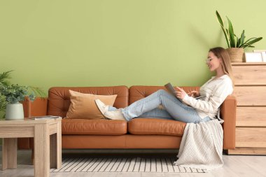 Evdeki kahverengi koltukta modern dizüstü bilgisayar kullanan güzel genç bir kadın.