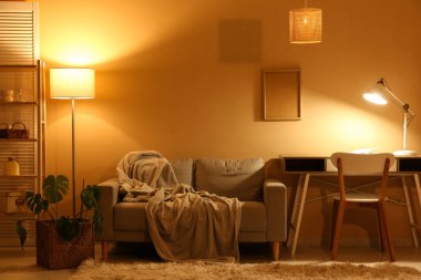 Gece oturma odasının içinde kanepe, raf ünitesi, parlayan lambalar ve işyeri