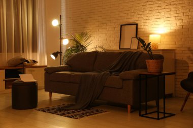 Gece oturma odasının içinde kanepe, puf, parlayan lambalar ve çiçekli.